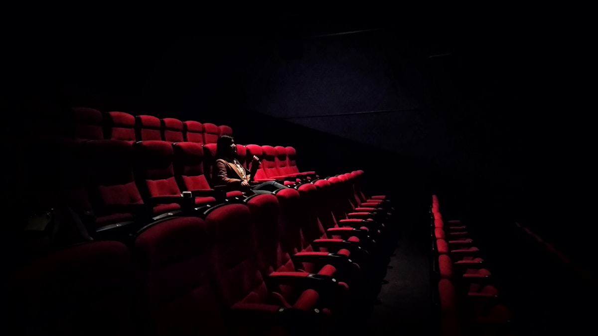 Butacas rojas de una sala de cine en penumbra, con la pantalla encendida al fondo